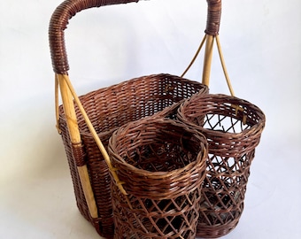 Könnte beinhalten: Ein brauner Picknickkorb aus Korbgeflecht mit einem Griff und zwei zylindrischen Haltern. Der Korb besteht aus gewebtem braunem Korbgeflecht und hat ein rechteckiges Fach. Die zylindrischen Halter sind offen gewebt.