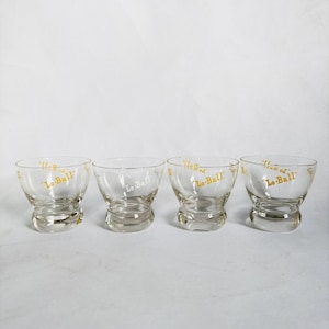Puede incluir: Cuatro vasos de vidrio transparente con forma de cuenco redondeado y una base gruesa tipo pedestal. El texto "Lo-Ball" está impreso en dorado en cada vaso. Los vasos están dispuestos en fila sobre un fondo blanco.