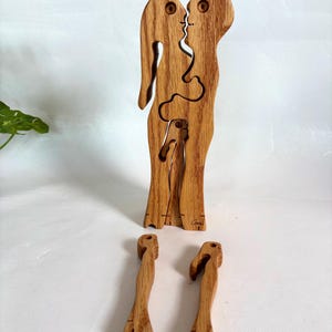 May include: A wooden puzzle depicting two figures kissing, with interlocking pieces. The puzzle is made of light brown wood and has a natural finish. Three separate pieces are also visible. The puzzle is a unique decorative item.