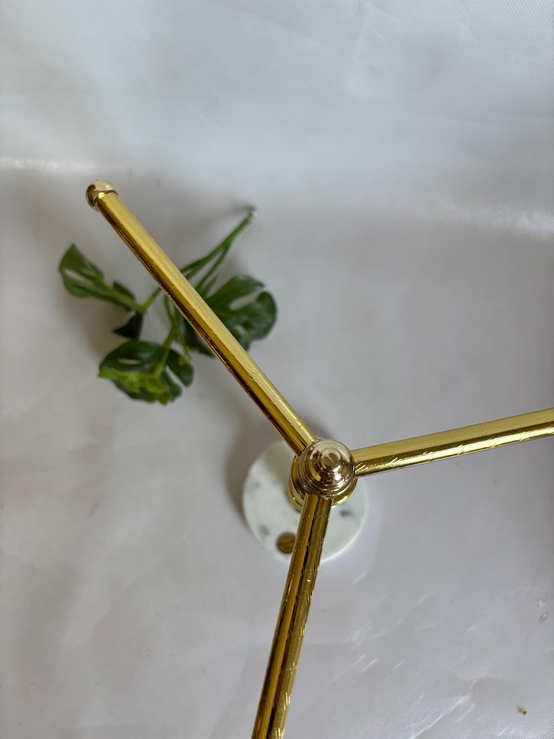 May include: A gold-colored metal decorative stand with a circular marble base and three arms extending outwards. The stand has a modern design and is suitable for displaying small items.