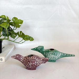 May include: Two bird-shaped decorative objects. One is a deep burgundy color with white dot and line details. The other is green with white etched patterns. Both have a small circular opening on top.