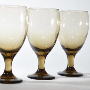 May include: Three clear glass wine goblets with a brown ombre effect. The goblets are arranged in a row from left to right.