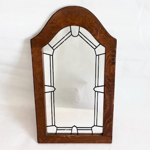 May include: A rectangular wooden mirror with a curved top. The frame is a medium brown color. The mirror has a black geometric design around the edges. The mirror is set against a white background.