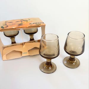 May include: Set of four brown glass shot glasses with a stemmed base. The glasses are packaged in a box with the word "Accent" printed on it.