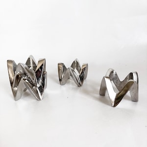 May include: A white ceramic mug with a black handle and the text "But First, Coffee" in a bold, black font. The mug is set against a blurred background, suggesting a cozy setting.