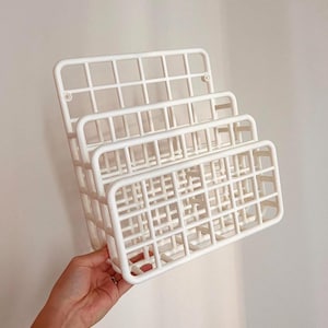 May include: White metal wall mounted organizer with three tiers. The organizer has a grid pattern and is perfect for storing small items.