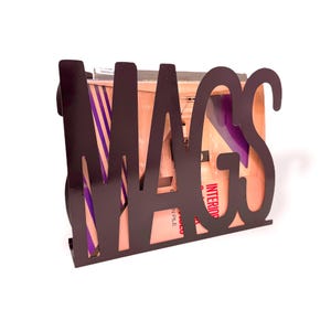 May include: A dark brown metal magazine holder with the word "MAGS" cut out. The holder contains magazines with visible text and colorful covers. The design is modern and suitable for home or office use.