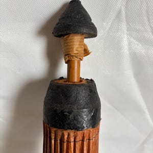 Puede incluir: Primer plano de un paraguas vintage. El paraguas presenta una parte superior negra en forma de cono y un mango de madera marr&oacute;n. El cuerpo del paraguas est&aacute; hecho de material plisado de color marr&oacute;n rojizo, con detalles en negro. El paraguas es un dise&ntilde;o cl&aacute;sico.