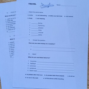 May include: Two sheets of white paper with travel-themed exercises. One sheet has fill-in-the-blank questions and matching exercises. The other sheet has multiple-choice questions. The word "TRAVEL" is at the top of one sheet, with a drawing of an airplane.