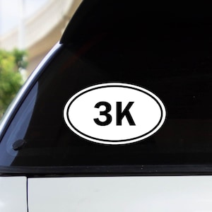 May include: A white oval sticker with black text that reads "3K" on a white car.