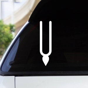 May include: White vinyl sticker of a religious symbol, a stylized representation of a sacred thread, on the back window of a silver car.