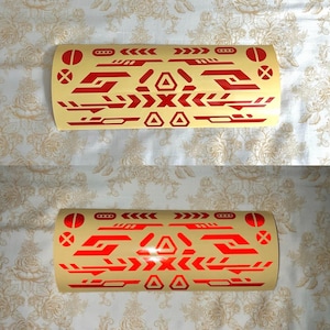 May include: Two red and beige decorative stickers with a geometric design. The stickers feature a series of arrows, triangles, and other shapes. The stickers are rolled up and ready to be applied.