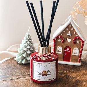 May include: Red glass diffuser bottle with a gold lid and black diffuser sticks. The bottle has a white label with the text "Christmas Spice" and a festive design.