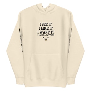 May include: A cream-colored hoodie with a black graphic that says "I see it I like it I want it I make a pattern" with a smiling emoji.