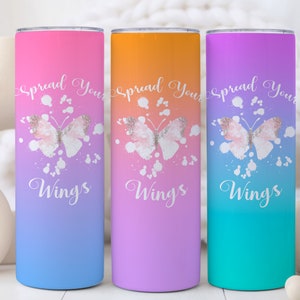 May include: Three stainless steel tumblers with a gradient ombre design. The tumblers feature a butterfly with glitter accents and the text "Spread Your Wings". The tumblers are pink, purple, and blue.