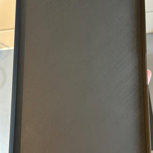 May include: A rectangular black tray with a textured surface and rounded corners. Four silver-colored rivets are visible, one in each corner. The tray appears to be made of a durable material.