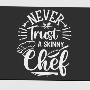 May include: Black rectangular kitchen mat with rounded corners. The mat features white text that reads "NEVER Trust A SKINNY Chef" with chef-related graphics. A chef's hat, a skillet, and a knife are also included in the design.