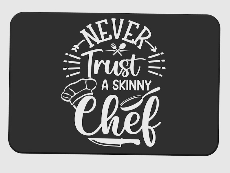 May include: Black rectangular kitchen mat with rounded corners. The mat features white text that reads "NEVER Trust A SKINNY Chef" with chef-related graphics. A chef's hat, a skillet, and a knife are also included in the design.