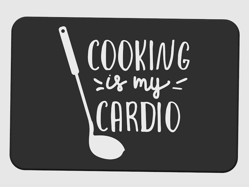 May include: Black rectangular kitchen mat with rounded corners. The mat features a white illustration of a ladle and the phrase "COOKING is my CARDIO" in a handwritten style font.