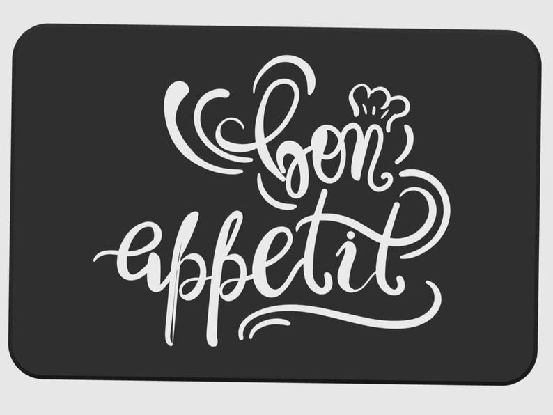 May include: A rectangular black kitchen mat with rounded corners. The mat features the words "Bon app&eacute;tit" in elegant white cursive script, with a chef's hat above the word "bon".