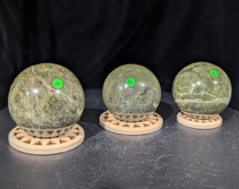 May include: Three green and white marble spheres on wooden stands. The spheres are polished and have a swirling pattern.