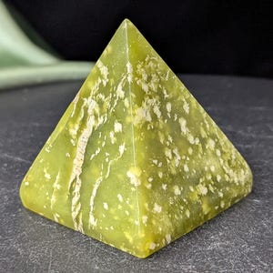 May include: A green pyramid-shaped crystal with white and light green markings. The crystal is smooth and polished.