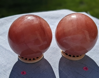 May include: Two large, polished, pink spheres on wooden bases. The spheres are made of rose quartz.
