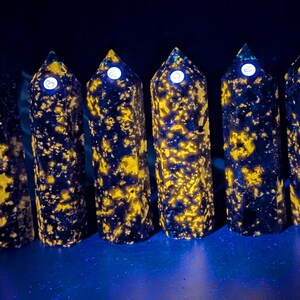 May include: Six polished black and yellow gemstone towers with white labels marked A through F. The towers are arranged in a row on a blue surface.