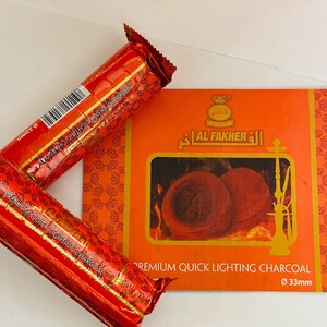 May include: Two red and gold packages of Al Fakher Premium Quick Lighting Charcoal, each with a diameter of 33mm. The packaging features a gold crown and the text "Al Fakher" in Arabic. The charcoal is shown burning in a hookah.