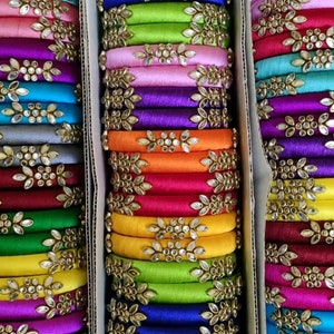 May include: A stack of colorful silk thread bangles with gold accents and rhinestones. The bangles are arranged in three columns and are all different colors, including red, green, blue, yellow, and purple.