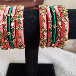 May include: A set of pink and green silk thread bangles with gold accents and clear and green gemstones.