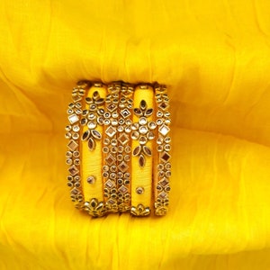 May include: A set of yellow silk bangles with gold and mirror embellishments. The bangles are stacked on top of each other and have a traditional Indian design.