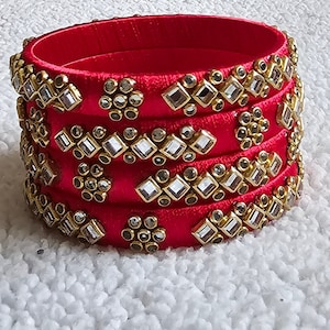 May include: A set of five red silk bangles with gold and clear rhinestone embellishments.