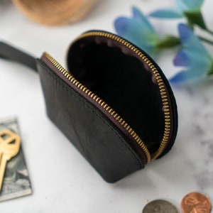 May include: A black leather coin purse with a gold zipper. The purse is open and the inside is visible. The purse has a small handle.