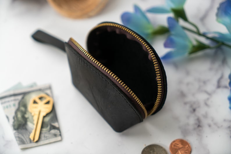 May include: A black leather coin purse with a gold zipper. The purse is open and the inside is visible. The purse has a small handle.