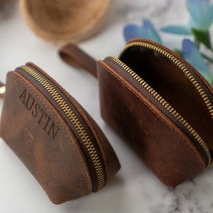May include: Two brown leather zippered pouches with gold zippers. One pouch has the name "Austin" embossed on the front.