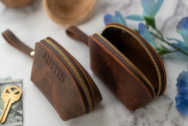 May include: Two brown leather zippered pouches with gold zippers. One pouch has the name "Austin" embossed on the front.