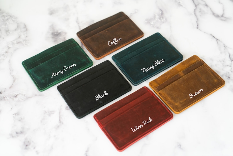 May include: A collection of leather cardholders in various colors: army green, coffee, navy blue, black, brown, and wine red. Each cardholder has a minimalist design with visible stitching and a slot for cards. The names of the colors are written in white script.