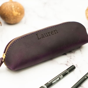May include: A purple leather pencil case with a gold zipper and the name "Lauren" engraved on the front.
