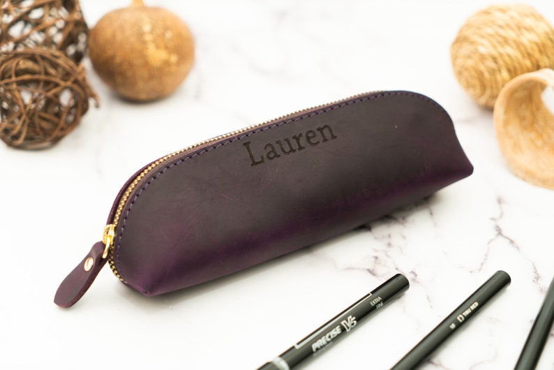 May include: A purple leather pencil case with a gold zipper and the name "Lauren" engraved on the front.