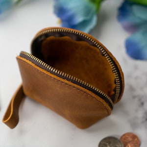 May include: A brown leather coin purse with a zipper closure and a strap. The purse is open and empty.