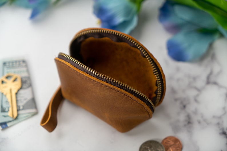 May include: A brown leather coin purse with a zipper closure and a strap. The purse is open and empty.