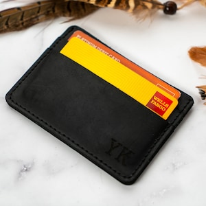 May include: A black leather card holder with two credit cards visible. The card holder has the initials "YK" embossed on the front. The cards are yellow and orange with the "Wells Fargo" logo.