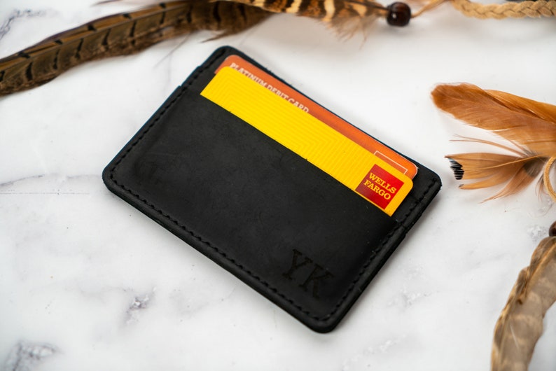 May include: A black leather card holder with two credit cards visible. The card holder has the initials "YK" embossed on the front. The cards are yellow and orange with the "Wells Fargo" logo.