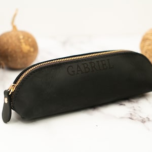 May include: Black leather pencil case with a gold zipper and the name "GABRIEL" embossed on the front.