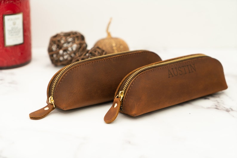 K&ouml;nnte beinhalten: Zwei braune Lederstiftetuis mit goldenen Rei&szlig;verschl&uuml;ssen. Das kleinere Etui tr&auml;gt den eingravierten Namen "AUSTIN".