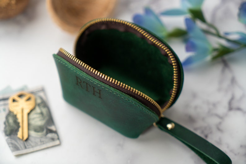 May include: A green leather zippered pouch with a brown leather strap and the initials "RTH" embossed on the front.