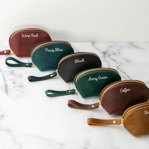 May include: Six half-moon shaped leather pouches with zipper closures and a strap. The pouches are in the colors wine red, navy blue, black, army green, coffee, and brown. Each pouch has a different color name embroidered on the front in white.