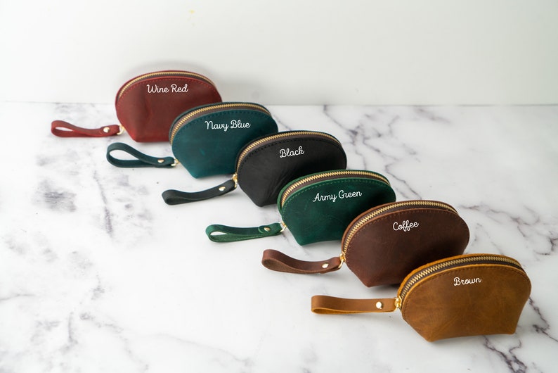May include: Six half-moon shaped leather pouches with zipper closures and a strap. The pouches are in the colors wine red, navy blue, black, army green, coffee, and brown. Each pouch has a different color name embroidered on the front in white.