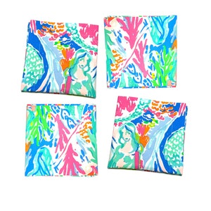 Puede incluir: Cuatro posavasos cuadrados de tela con un diseño abstracto y colorido. El patrón presenta una sirena, corales y otros elementos acuáticos en tonos azules, rosas, verdes y naranjas. Los posavasos están hechos de tela duradera.